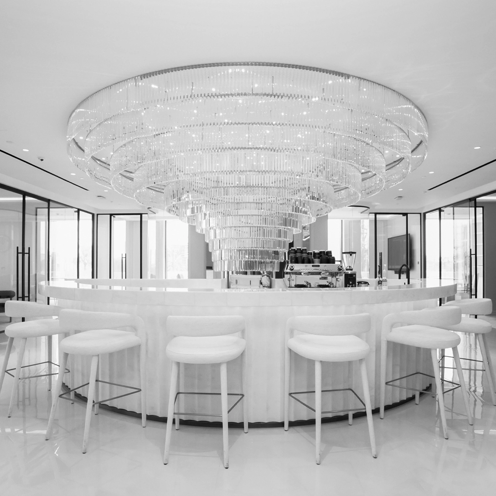 Modern office café with a curved counter, sculptural chandelier, and glass meeting rooms